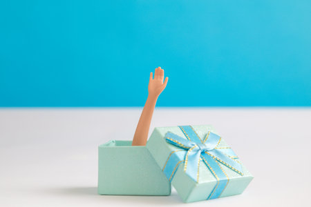 Doll arm out of gift box against blue background minimal creative holiday concept.