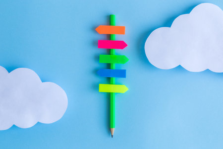 Flat lay of directions sign made of pencil with colorful blank sticky notes and paper clouds against...