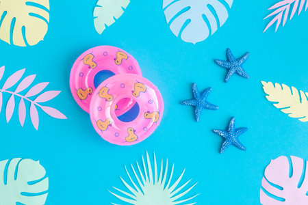 Flat lay of swimming floats with sea stars and colorful tropical leaves against blue background...