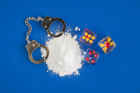 Flat lay composition of cocaine with handcuffs and dices against blue background minimal creative concept.の写真素材