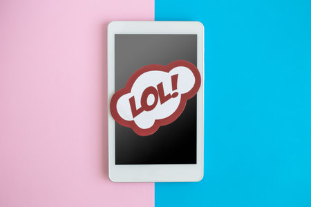 Flat lay of digital tablet device or mobile phone with lol text in speech bubble against pastel background minimal technology creative concept.の写真素材