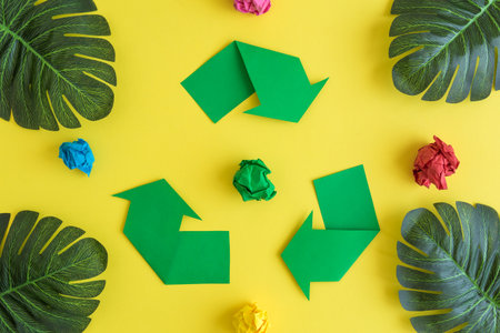 Green triangular eco recycle icon with monstera leaves with crumpled paper on yellow background minimal ecology creative concept.の写真素材