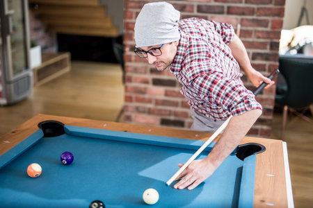 Fashionable hipster guy playing pool billiard game at the office chill room.