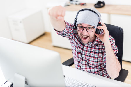 Cheerful modern man with headphones sitting at the desk and working on his computer.の写真素材