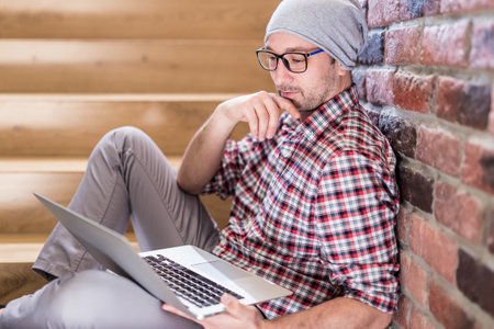 Modern hipster guy sitting on stairs and using laptop.の写真素材