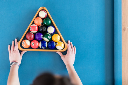 High angle view of female holding triangle wooden rack with pool balls on billiard table. Space for...
