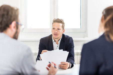 Portrait of young businessman discussing with his colleagues at the desk in meeting or conference room.