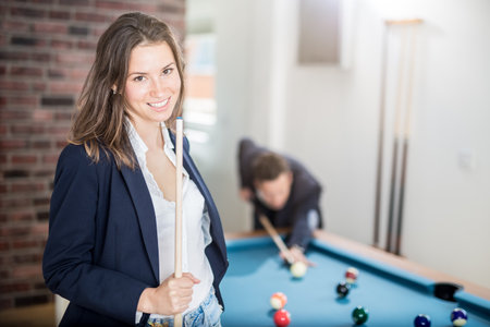 Portrait of beautiful billiard female player holding a cue stick and fashionable man aiming the ball at the pool table.の写真素材