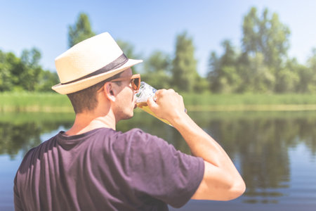 Rear view of young man wearing straw hat and drinking beer against beautiful nature.の写真素材