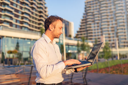 Successful businessman using laptop against modern buildings in the background.の写真素材