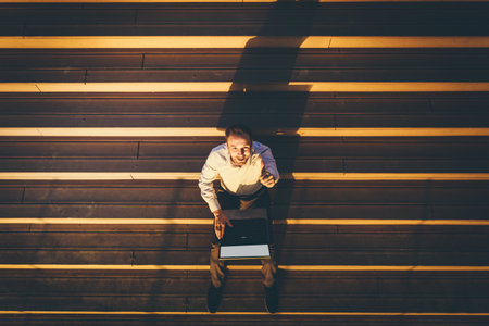 Top view of business professional with thumbs up using blank screen laptop and sitting on outdoor steps.の写真素材