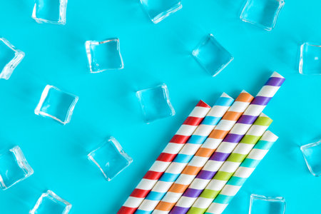 Flat lay of colorful drinking straws and ice cubes against blue background minimal creative summer and drink concept.の写真素材