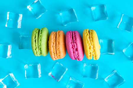 Flat lay of colorful macaroons and ice cubes against blue background minimal sweet food and drink creative concepts.の写真素材