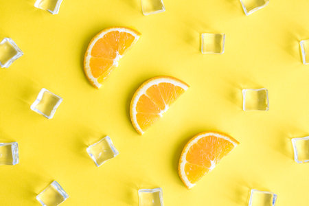 Flat lay of orange fruit slices and ice cubes against yellow background minimal creative summer...