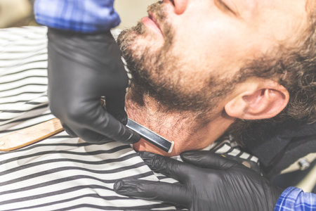 Close-up hands of barber holding razor and shaving a client.