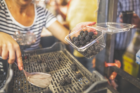 Female seller putting blackberries in plastic container at street market.