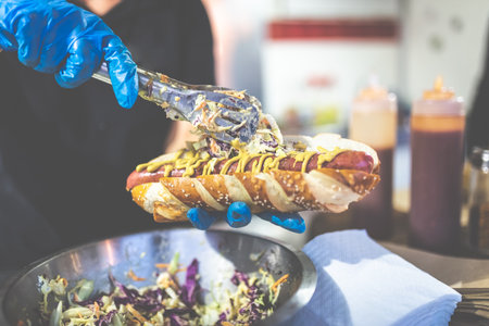 Close up of chef hands adding vegetables on fresh hot dog with grilled sausage.の写真素材