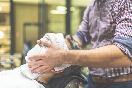 Barber preparing man face for shaving with hot towel in barber shopの写真素材