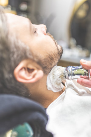 Fashionable man client during beard shaving in barber shop.の写真素材