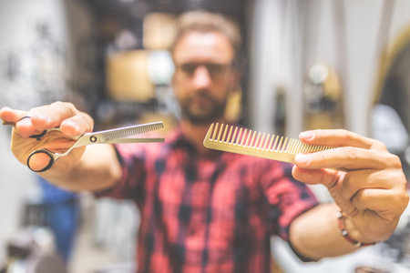 Modern barber holding comb and scissors at barbershop.の写真素材