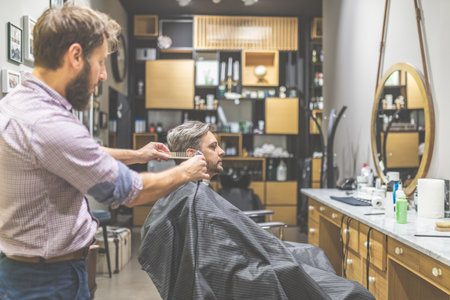 Professional barber styling hair of his client by using comb and clipper.の写真素材