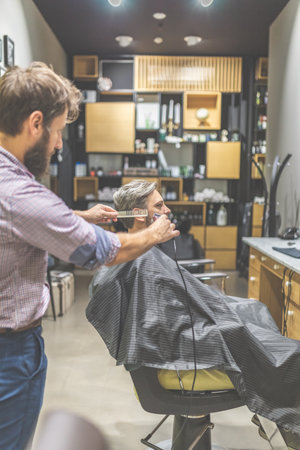 Professional barber styling hair of his client by using comb and clipper.の写真素材