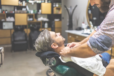 Hairdresser preparing client for shaving with towel. Man visiting barber shop.の写真素材