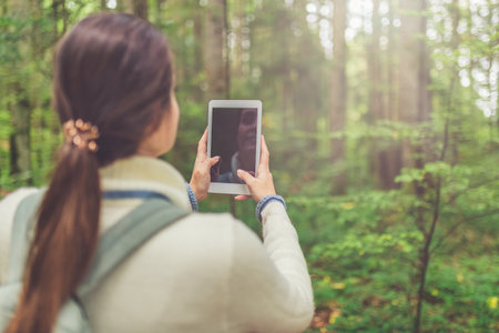 Young female holding blank screen digital tablet device against beautiful forest trees. Nature and technology concept.の写真素材