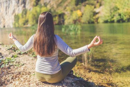 Young woman doing yoga and meditating at lake coast. Relax in nature.の写真素材