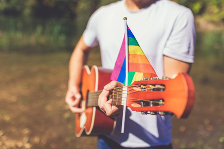 Close up of guitarist playing acoustic guitar with lgbt rainbow flag in nature. Music and freedom...