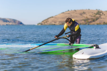 Sportsman preparing his windsurfing equipment in shallow water.