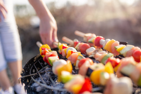 Close up of young female preparing mixed vegetable and chicken meat skewers on barbecue grill outdoors.の写真素材