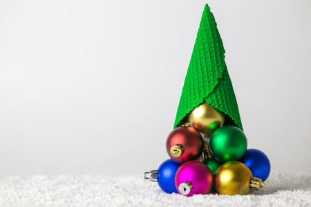 Ice cream cone with colorful baubles in form of Christmas tree in snow minimal creative holiday concept. Space for copy.の写真素材