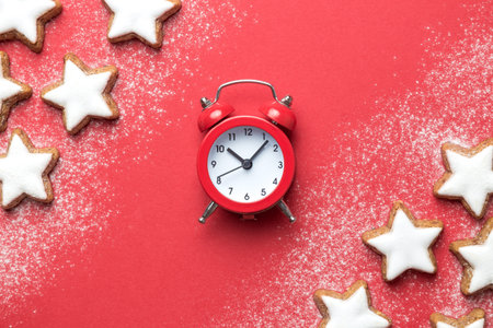 Flat lay of christmas star cookies and alarm clock on red background minimal creative concept....