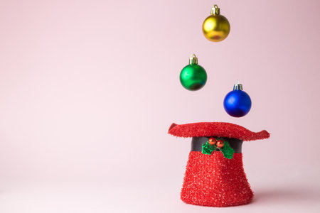 Multicolored baubles falling in red holiday hat, christmas abstract on rose. Space for copy.の写真素材