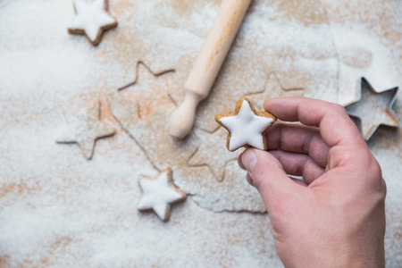 Close up of man hand holding star shape cookie against cutters, dough, rolling pin and biscuits in the background.の写真素材