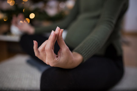 Close up of pregnant woman exercising yoga lotus position at home next to christmas tree.の写真素材