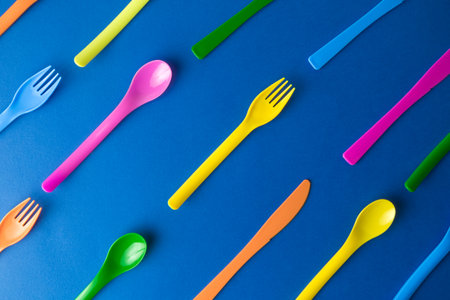Flat lay of colorful plastic disposable forks,spoons and knives pattern on classic blue background...