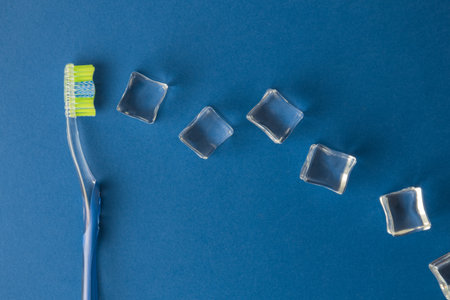 Flat lay of plastic toothbrush and ice cubes against classic blue background minimal creative...