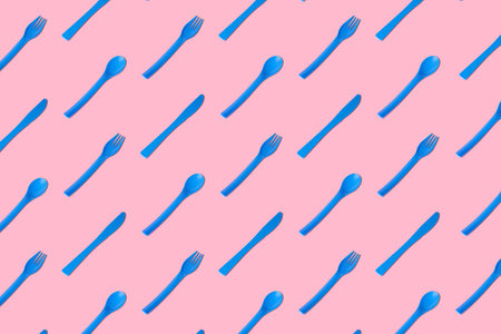 Flat lay of blue plastic disposable forks,spoons and knives pattern on pastel pink background minimal creative concept.の写真素材
