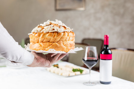Close up of hand holding traditional orthodox bread next to wine at the table.の写真素材