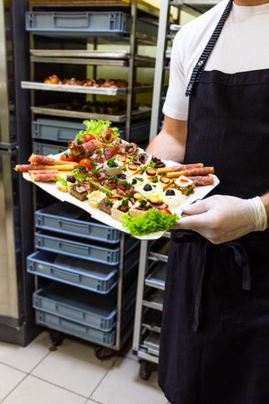 Chef or waiter holding platter full of fresh canapes finger food snacks for buffet meal at restaurant.の写真素材