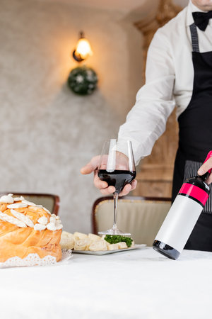 Waiter holding glass and bottle of wine next to traditional orthodox bread at home or restaurant table.の写真素材