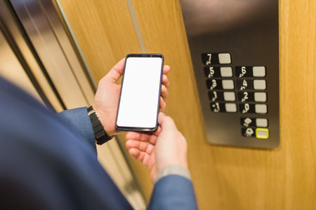 Close up of businessman using blank screen smartphone in elevator. Business and office building meeting concept.の写真素材
