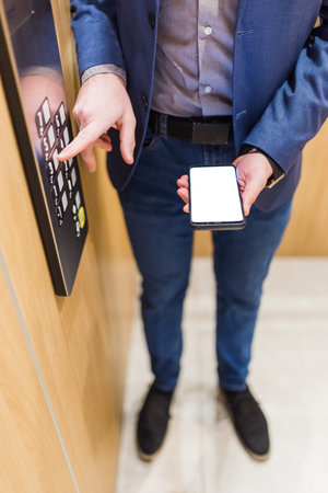 Man hands holding blank screen mobile phone while using elevator control panel.の写真素材