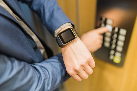 Close up of businessman looking at blank screen smart watch and pressing elevator button. Business and office building meeting concept.の写真素材