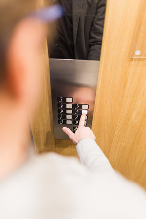 Close up of businessman pressing button in modern wooden and steel elevator.の写真素材