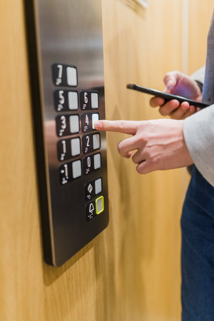 Close up of businessman using smartphone and pressing elevator button. Business and office building meeting concept.の写真素材