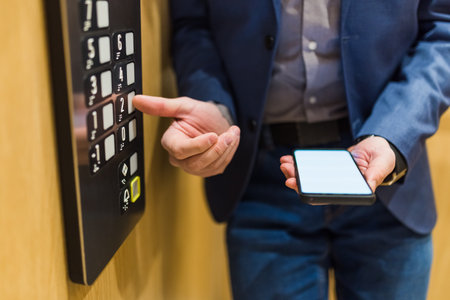 Man hands holding blank screen mobile phone while using elevator control panel.の写真素材