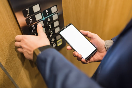 Close up of businessman using blank screen smartphone and pressing elevator button. Business and office building meeting concept.の写真素材